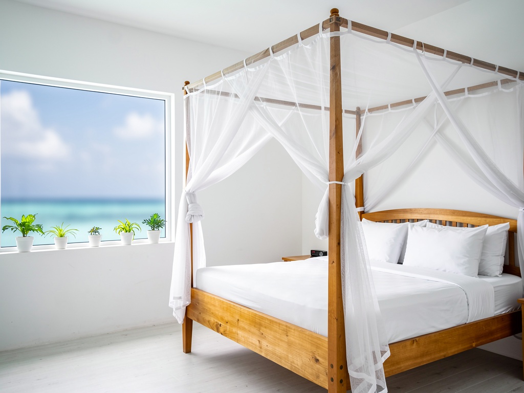 Clean white-walled guesthouse room in a Maldives local island with four-poster bed